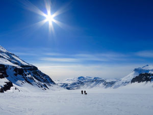 Det är säkert enklare att orka när det ser så här vackert ut. Här en bild från en av Fridas tidigare utfärder. Två personer som skidar. Runt omkring finns berg och snö. Himlen är blå och solen skiner.