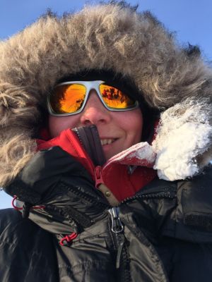 Frida Pelin - snart i en Grönlandsblogg nära dig. Kvinna med solglasögon och en stor jacka med pälskantad huva.