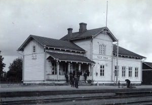 Vuonna 1869 valmistunut asemarakennus edustaa 1800-luvun lopulle tunnusomaista uusrenessanssia. Kuvassa junaa odotellaan Pulsan asemalla vuonna 1908 tai 1909. Mustavalkoinen arkistokuva vanhasta puisesta rautatieasemasta, edessä henkilöitä odottamassa, 1900-luvun alkua.