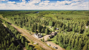 Pulsan asemalle varattiin tavallista suurempi alue keskellä eteläkarjalaista korpiseutua. Ilmakuva vanhasta rautatieasemasta, ympärillä metsää, taustalla taivas.