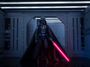Darth Vader med sin ljussabel - inte en praktisk effekt. En leksaksfigur föreställande Darth Vader från Star wars. Han står framför en port, ser ut att vara en rymdbas. Han håller sin röda ljussabel i handen.
