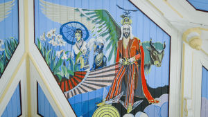 Kirkasvärisiä kattomaalauksia kirkon sisäkatossa, jeesus, eri etnisiä ryhmiä edustavia enkeleitä.