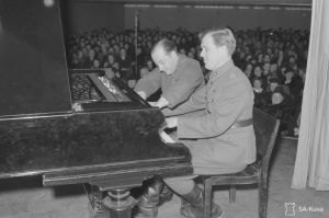 Kevättalvella 1943 ihmiset istuivat ilmahälytysten takia takit päällä konsertissa. Kuvassa luutnantti Nils-Eric Fougstedt ja sotamies George de Godzinsky. He soittivat nelikätisesti konservatorion eli Sibelius-Akatemian salissa järjestetyssä Toivekonsertissa 25. maaliskuuta 1943. Luutnantti Fougstedt ja sotamies Godzinsky soittavat nelikätisesti pianoa Konservatorion salissa Toivekonsertissa 25.3.1943.