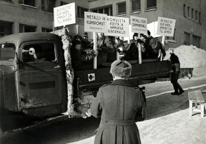 Koululaisia kevättalvella 1942. Koululaisia kuorma-auton lavalla kädessään iskulausekylttejä: "Romuista aseita ja ammuksia rintamalle."