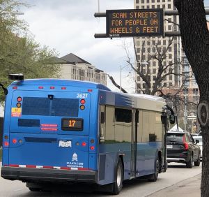 I förgrunden en blå buss på en gata i Austin i Texas. I hakgrunden höghus.