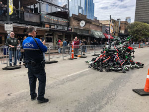 En hög med elektriska sparkcyklar på en gata i Austin i Texas. En polis fotograferar med mobiltelefon.