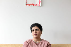 Azra Tayyebi istuu sohvallaan laajassa kuvassa. Pään yläpuolella näkyy hieman punaista piirustusta.