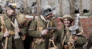 Valokuva ensimmäisen maailmansodan ajalta. Kolme miestiä seisoo rivissä tiiliseinää vasten aseiden kanssa, ja yksi miehistä osoittaa käsiaseella toista. Peter Jacksonin dokumenttielokuvasta They shall not grow old.