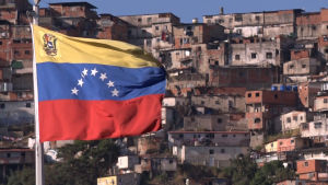 Venezuelasta on varastettu satoja miljardeja valtion rahoja. Köyhiin kortteleihin ei tule vettä, sähköäkin vain satunnaisesti. Venezuelan lippu, taustalla slummia.