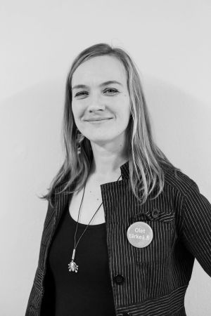 Minna Saunders berättar att offentliga sektorn i Åbo nu erbjuder också annat än akutvård för papperslösa. En svartvit bild på Minna Saunders. Hon har en långrandig jacka med en knapp på. Knappen har texten Olet tärkeä.fi.