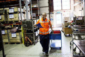 Sami Heinonen iklädd orange väst drar en kärra i fabrikshall.