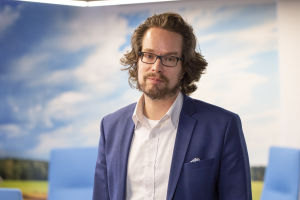 Specialforskare Juha-Matti Katajajuuri tycker att det är viktigt att de stora butikskedjorna gör sitt för att minska på matsvinnet. "Då är det lätt för konsumenterna att tänka att de egna gärningarna har en betydelse", säger han. En man i vit skjorta och blå kostym står framför en vägg som ser ut som en blå himmel. Han tittar in i kameran.