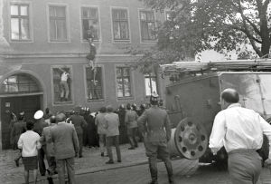 En del flyktförsök var mer synliga än andra. Här är ett försök till flykt i september 1961. En svartvit bild från 1960-talet. Människor har samlats ute på gatan framför en byggnad och tittar på tre människor som försöker klättra in och ut genom fönster på väggen.