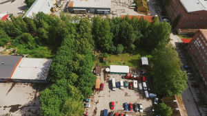 Ilmakuva pienteollisuusalueesta, keskellä viheralue, jota ympäröi parkkipaikka, katu sekä punatiiliset rakennukset.