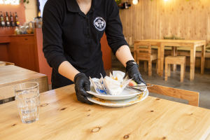 Arbetshälsoinstitutet rekommenderar att bland annat servitörer använder sig av engångshandskar. Thai Street Foodin työntekijä kerää lautasia pöydästä.
