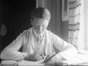 Tauno keskittyy kirjoituspöydän ääressä. Teini-ikäinen Tauno Hannikainen on syventynyt kirjoitustehtävään pöydän ääressä. Kuva noin vuodelta 1910.