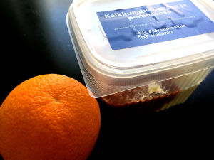 Ungefär en fjärdedel av Helsingfors skolbarn åt skollunch under de två senaste veckorna. En förpackning med skolmat. Bredvid plastlådan sitter en apelsin.