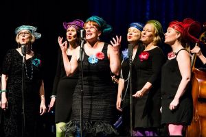 Merry Ladies ja Olohuoneorkesteri Savoy-teatterin lavalla 2017. Lääkärimuusikot estradilla - konsertti tieteen hyväksi. Tilannekuva: Merry ladies tyylikkäinä mustissa mekoissa ja iloisissa hatuissa laulamassa lavalla