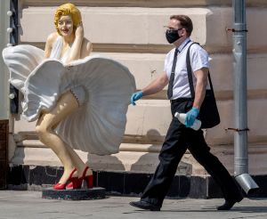 Också caféer har fått öppna i Moskva. Manlig person med ansiksskydd går förbi Marilyn Monroe-staty.