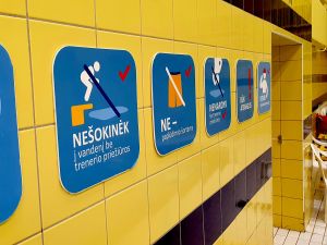 Varningsskyltarna är placerade precis bredvid dörren till omklädningsrummet. Varningsskyltar som bland annat förbjuder hopp i bassängen på väggen i en litauisk simhall.