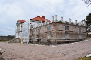 Den stora vita huvudbyggnaden på söderlångvik gård omgiven av byggställningen och med den vita rappningen nerknackad på flyglarna så att den gråröda tegelväggen är blottad.