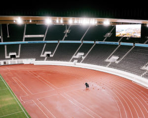 Palloja kerätään kentällä. Yksi ihminen noukkii kymmeniä maahan levittäytyneitä palloja Olympiastadionilla.