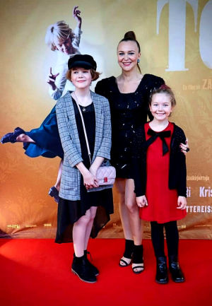 Andrea på galapremiären av filmen Tove, tillsammans med sina brorsdöttrar Svea och Selma. En festklädd mamma med sina festklädda barn på röda mattan framför en filmplansch.