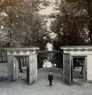 Symmetrinen kuva Helsingin observatorion avatuista porteista, joiden edessä mukulakiveyksellä seisoo poika tummassa puvussa.