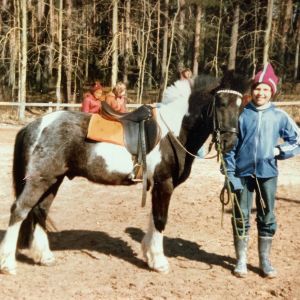 11-vuotias Pia Lindy seisoo ponin vieressä ratsastuskentällä, taustalla metsää.