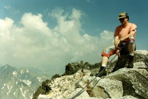 Ville Keynäs harrastaa vuorikiipeilyä. Keynäs kiipeämässä Gerlachvuorella Slovakiassa vuonna 1996. Vuorikiipeilyä harrastava mies istuu kalliolla. Hän on kiinni turvavaljaassa. Päässä on lippalakki.