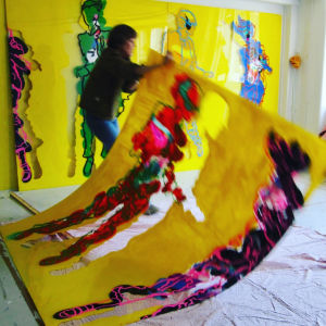 Kirsti Tuokko nostaa suurta keltaista maalausta lattialta.