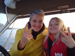 Puoliso Corinne ja tytär Tilla veneessä matkalla Inkoon ulkosaaristoon, jossa Corinnen suvulla on oma saari. Moottoriveneellä matka saarelle kestää noin 20 minuuttia, mutta reitti on varsinkin loppuvaiheissa hyvin karikkoinen. Vene on usein lastattu täyteen, mm. siksi, että juomavesi pitää tuoda mantereelta. Corinne ja Tilla katsovat kameraan ja näyttävät voitonmerkkiä.