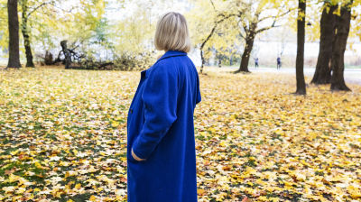 Nainen sinisessa takissa seisoo selin kameraan ja katsoo syksyiseen maisemaan.