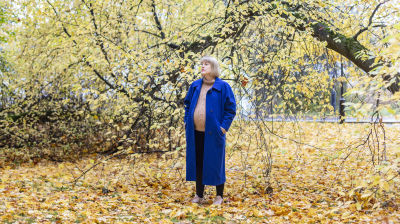 Raskaana oleva nainen seisoo puistossa pudonneiden lehtien keskellä.