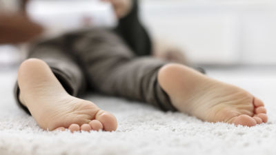 Pienen lapsi makaa vaalealla pehmeällä matolla mahallaan jalkapohjat kohti kameraa.