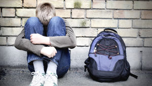 Mobbning är fortfarande ett stort problem bland unga som redan är utanför. En ensam pojke sitter lutad mot en vägg med huvudet mot knäna.