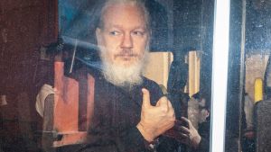 En skäggig Julian Assange fotograferad genom ett bilfönster.