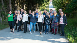Sukulaiset tulivat yllättämään Eijan Tuhkimotarinoiden kuvauksiin. Sukulaiset näyttävät peukkua kameralle. He seisovat rivissä kuusien reunustamalla tiellä.