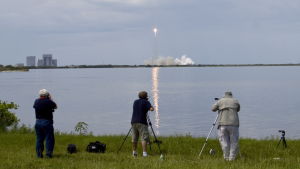 Falcon-9 på väg upp vid Cape Canaveral Fotografer på strand ser uppskjutning av Falcon 9-bärraketen i stort rökmoln på Cape Canveral