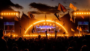 På Roskilde-festivalen fcik Gustafsson improvisera ett radioprogram i en diktafon. Orangegul stämningsbild på natten på Rokilde-festivalen. Silhuetter av publik med flaggor framför orangea huvudscenen under Eminems gig.