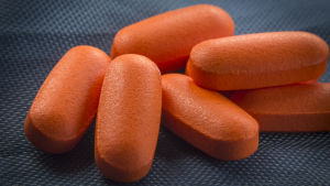 Röda piller förknippas med högre blodtryck. Orange tabletter mot en mörk bakgrund