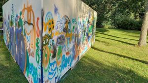 Enligt Marianne Liitelä har Pojoborna inte reagerat negativt på gatukonstväggen. En triangelformad vägg eller ett plank som placerats ute på en gräsmatta. Det är gatukonst, graffiti målat på väggen.