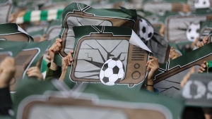 Många supportrar är kritiska till att fortsätta säsongen. (Arkivbild från 2018 då fansen protesterade mot betal-tv). Affischer med trasiga teverutor och en fotboll mot rutorna lyfts upp i ett stort hav av händer.