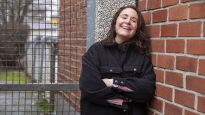 Mikaela är mycket gladare nu när hon jobbar i affär. En kvinna med långt hår står lutad mot en tegelvägg.