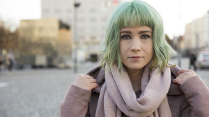 Henna Johansdotter förliknar känslan att ge ut en bok med en graviditet. Hon bearbetade känslorna genom att skriva dikter. Många hörde av sig efter att ha läst dikterna med kondoleanser, eftersom de trott att hon fått missfall. Henna tittar rakt in i kameran. Hon står på ett torg och håller i jackans huva som hon fällt ner. Hon har turkosa hår och stark kajal målad kring ögonen.