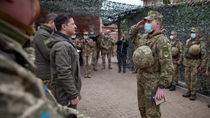 Ukrainas president Volodomyr Zelenskyj tillsammans med en grupp soldater Ukrainas president Volodomyr Zelenskyj står tillsammans med en grupp soldater framför honom står en soldat i ansiktmask som gör honnör.
