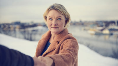 En blond dam i ett vintrigt landskap håller någons hand i förgrunden.