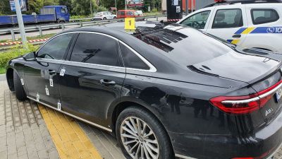 en svart bil står parkerad på en parkeringsplats. Bilen har flera skotthål.
