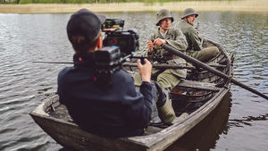Jonny Forsman filmar en scen i Öby. Två soldater i en gammal träeka. De är skådespelare. I båten sitter också en person i nutida kläder med filmkamera på axeln.