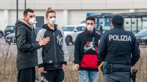 Många vill komma i kontakt med nödcentralen. En polis står och pratar med personer i Italien som bär munskydd till följd av coronaviruset.
